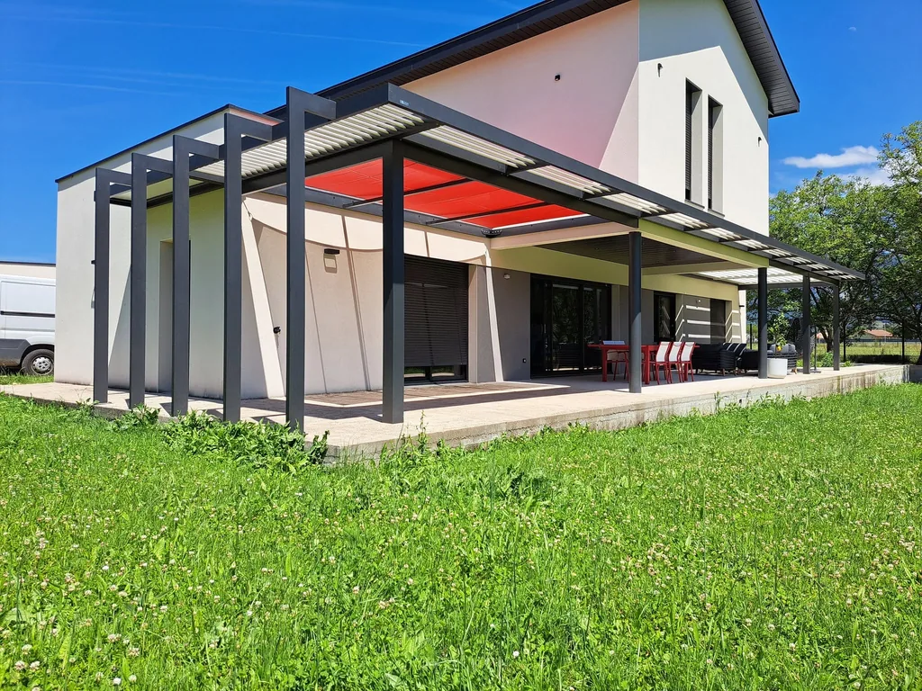 Terrasse couverte à Saint-Marcellin : pergola bioclimatique à lames orientables, voile d’ombrage rouge et tubes verticaux, structure aluminium anthracite